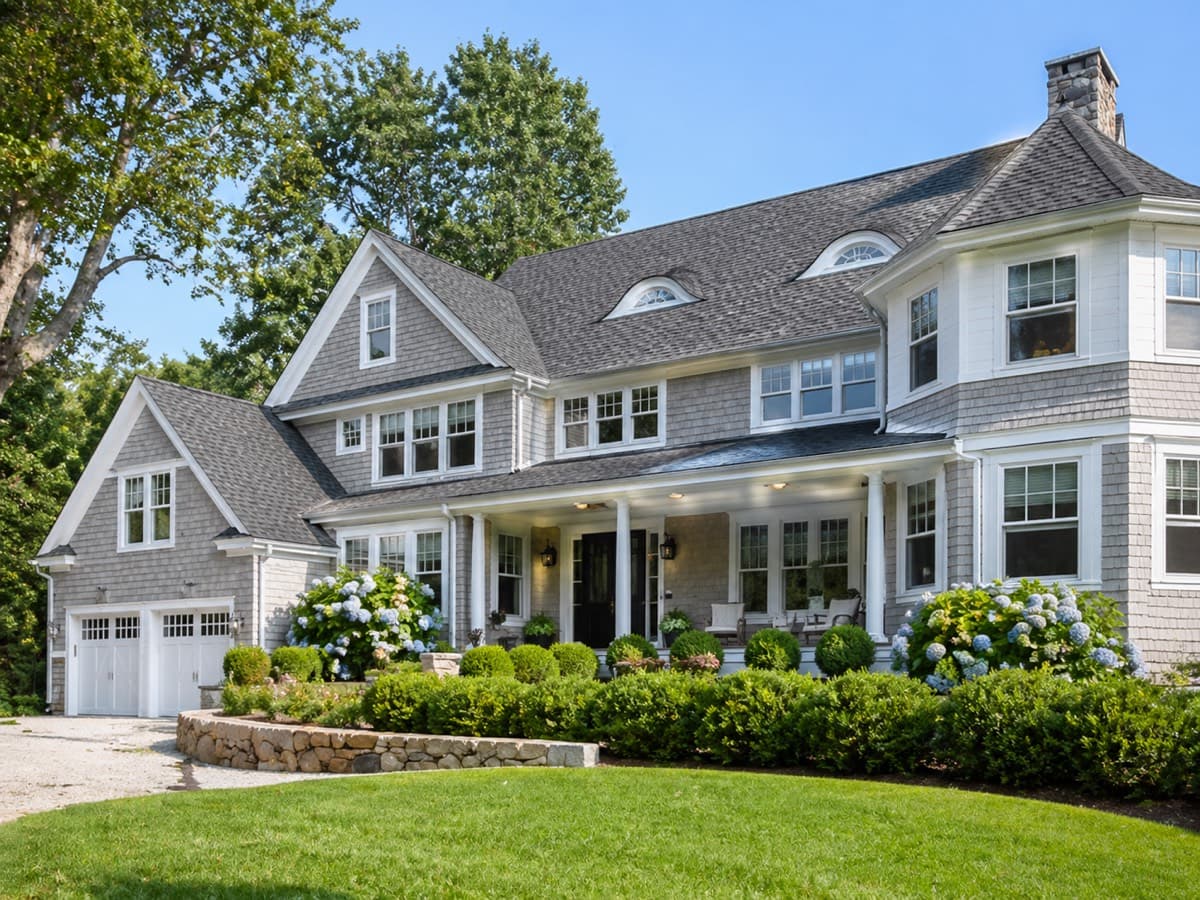 Large gray shingle-style home with hydrangeas and stone wall